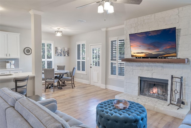 living area featuring baseboards, visible vents, ceiling fan, light wood-type flooring, and a fireplace