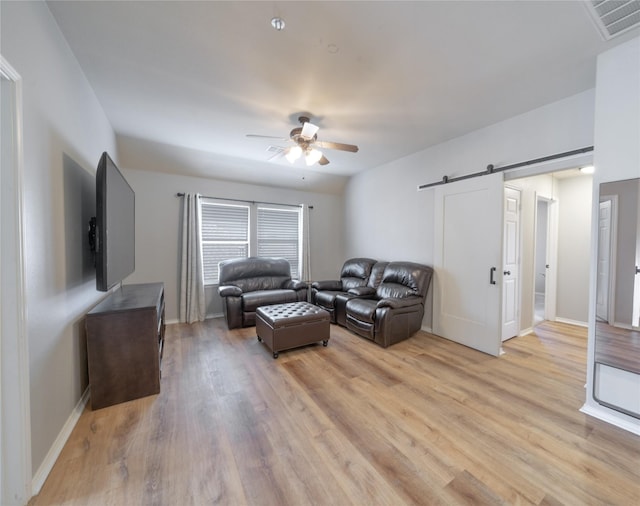 living room with light wood finished floors, a barn door, visible vents, baseboards, and a ceiling fan