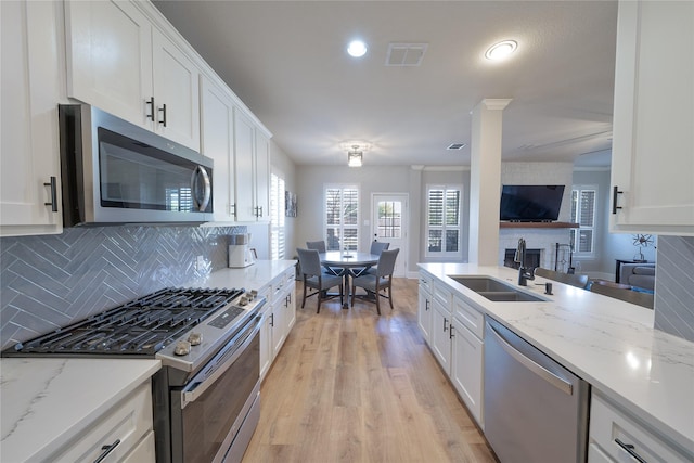 kitchen featuring tasteful backsplash, visible vents, white cabinets, stainless steel appliances, and a sink