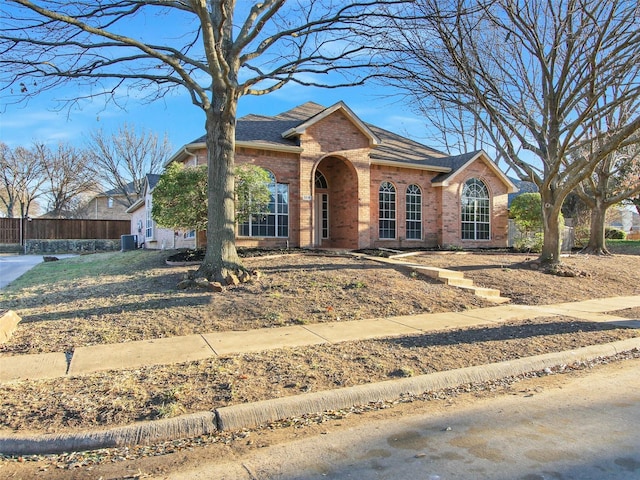 view of front of property with central AC unit, roof with shingles, fence, and brick siding