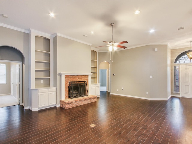 unfurnished living room with arched walkways, dark wood-style flooring, a brick fireplace, and baseboards