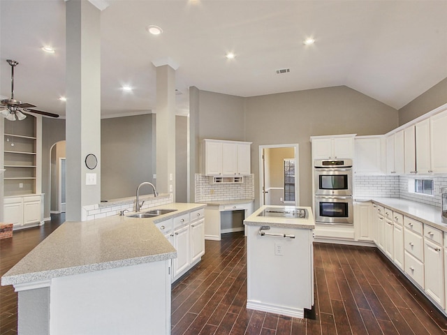 kitchen featuring arched walkways, stainless steel double oven, dark wood-type flooring, a sink, and a center island