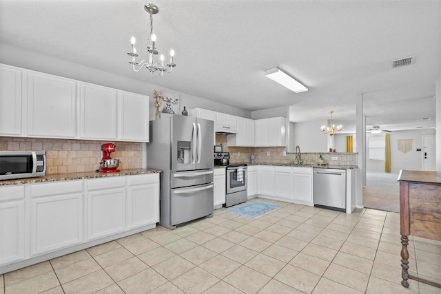 kitchen featuring decorative backsplash, stone counters, stainless steel appliances, under cabinet range hood, and ceiling fan with notable chandelier