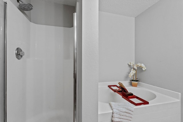 bathroom with a shower stall, a textured ceiling, and a bath