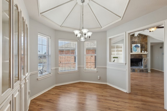 unfurnished dining area with lofted ceiling, wood finished floors, an inviting chandelier, a fireplace, and baseboards