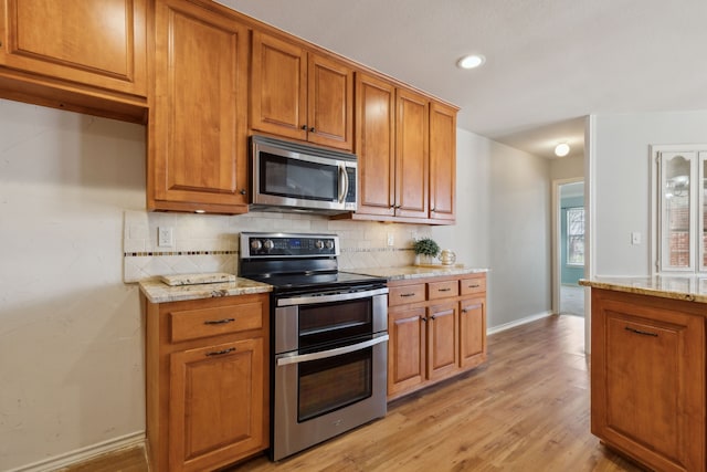 kitchen with light stone counters, backsplash, appliances with stainless steel finishes, and brown cabinetry