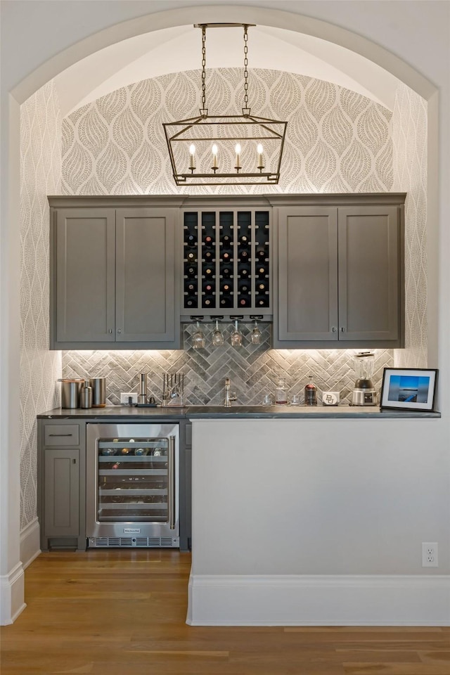 bar featuring wallpapered walls, beverage cooler, wood finished floors, and decorative light fixtures