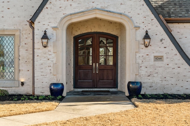 view of exterior entry featuring french doors, roof with shingles, and stucco siding