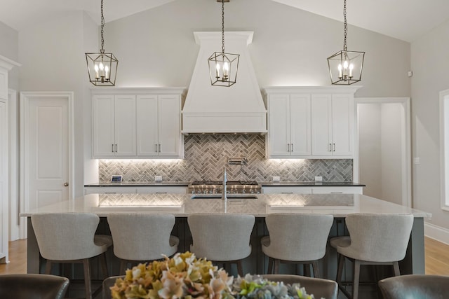 kitchen featuring high vaulted ceiling, premium range hood, wood finished floors, white cabinetry, and a center island with sink