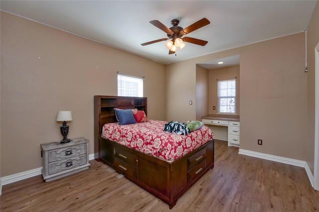 bedroom featuring light wood-style floors, multiple windows, and built in desk