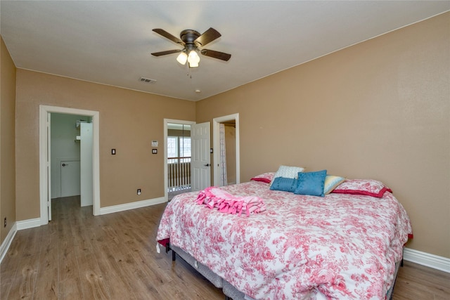 bedroom featuring baseboards, visible vents, ceiling fan, wood finished floors, and a walk in closet