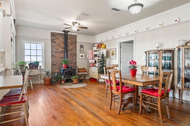 dining area with a wood stove, wood finished floors, visible vents, and crown molding