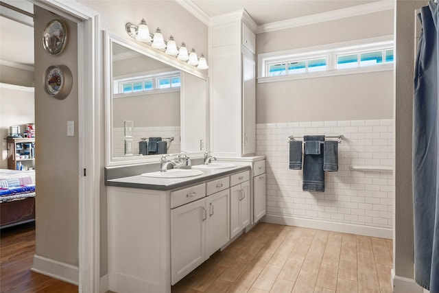 ensuite bathroom featuring crown molding, wainscoting, a sink, ensuite bath, and wood finished floors