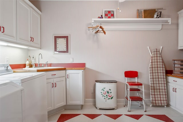 kitchen featuring light tile patterned floors, wallpapered walls, white cabinets, washer and dryer, and a sink