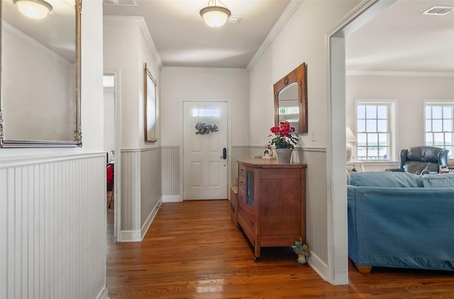 doorway to outside featuring crown molding, visible vents, wood finished floors, and wainscoting