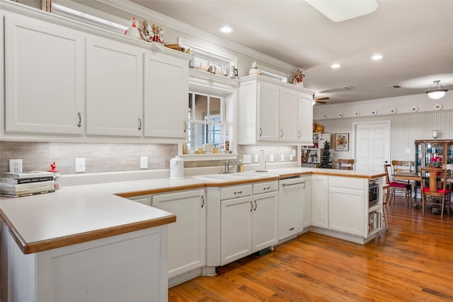 kitchen with a peninsula, white dishwasher, white cabinetry, and a sink