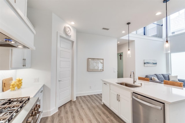 kitchen with hanging light fixtures, stainless steel appliances, light wood-style floors, white cabinetry, and a sink