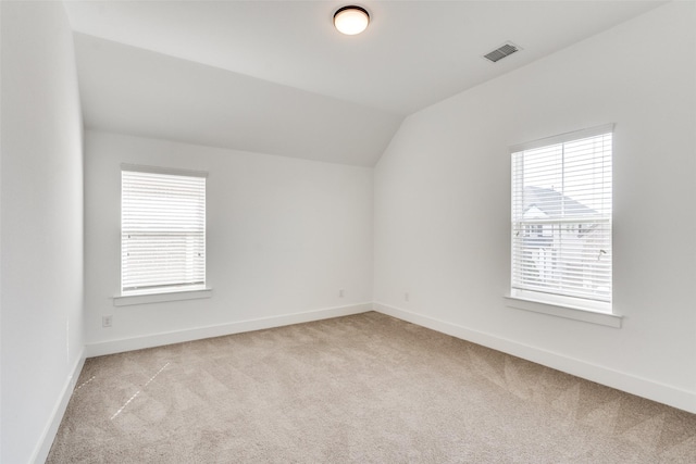 empty room featuring carpet, visible vents, vaulted ceiling, and baseboards