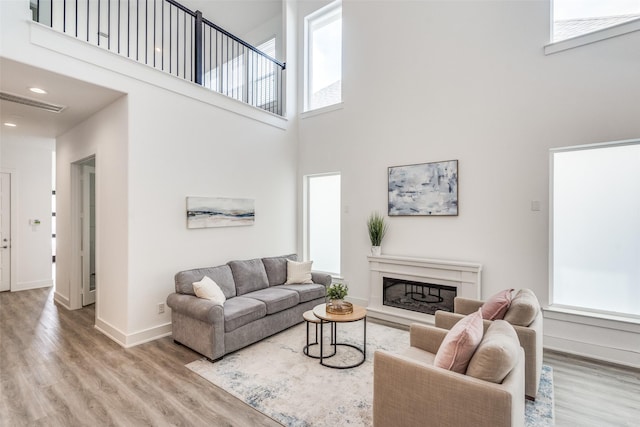 living area with a fireplace, recessed lighting, a towering ceiling, wood finished floors, and baseboards