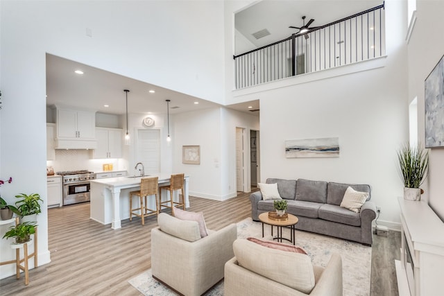 living room with light wood-style flooring, visible vents, ceiling fan, and baseboards