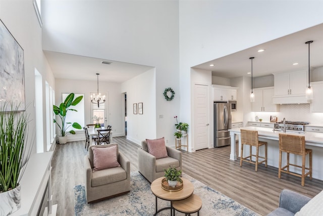 living area with visible vents, baseboards, a towering ceiling, light wood-style flooring, and a chandelier