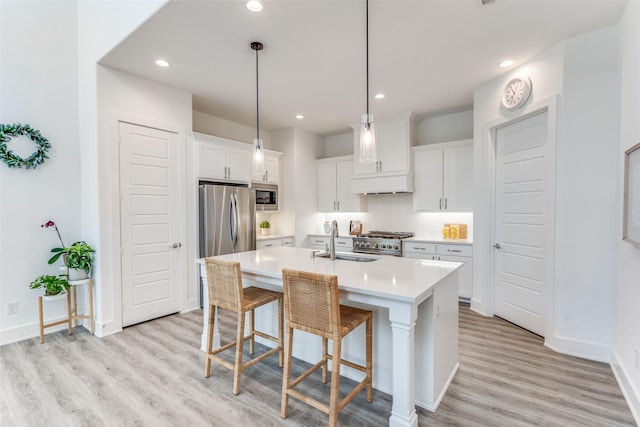 kitchen with a breakfast bar area, stainless steel appliances, a sink, light countertops, and light wood-type flooring