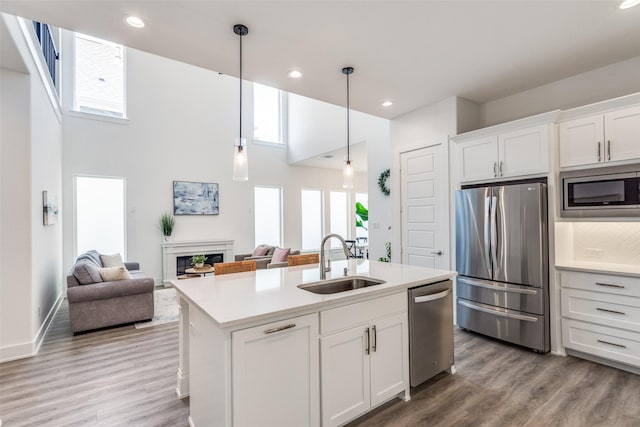 kitchen featuring white cabinets, stainless steel appliances, light countertops, a fireplace, and a sink