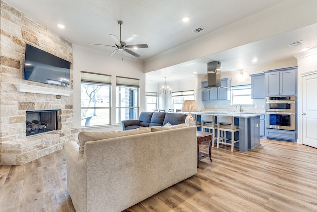 living area with ornamental molding, visible vents, a fireplace, and light wood finished floors