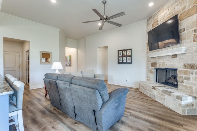 living room featuring a fireplace, wood finished floors, a ceiling fan, baseboards, and ornamental molding