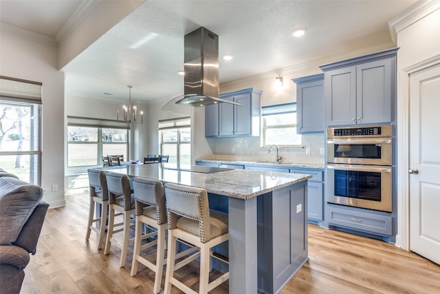 kitchen with ornamental molding, a center island, light stone countertops, island exhaust hood, and double oven