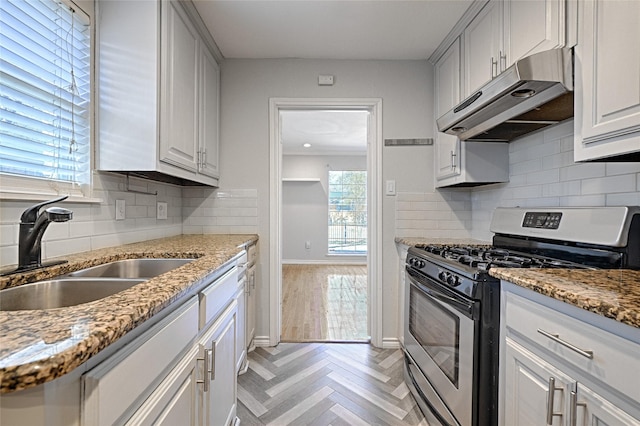 kitchen featuring baseboards, a sink, light stone countertops, under cabinet range hood, and stainless steel gas range oven