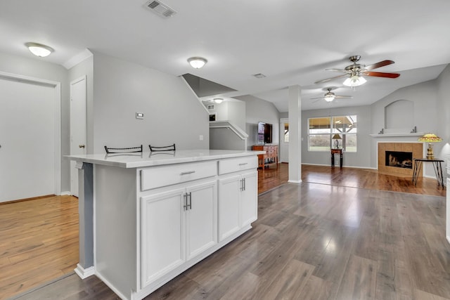 kitchen with visible vents, a tiled fireplace, open floor plan, wood finished floors, and light countertops