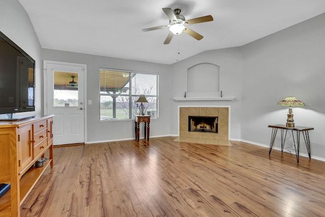 living area featuring lofted ceiling, light wood finished floors, baseboards, and a tiled fireplace