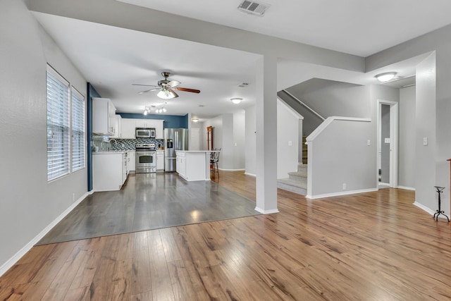 unfurnished living room with visible vents, baseboards, wood-type flooring, ceiling fan, and stairs