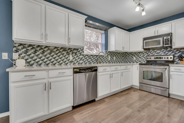 kitchen featuring tasteful backsplash, light countertops, appliances with stainless steel finishes, white cabinetry, and light wood-type flooring