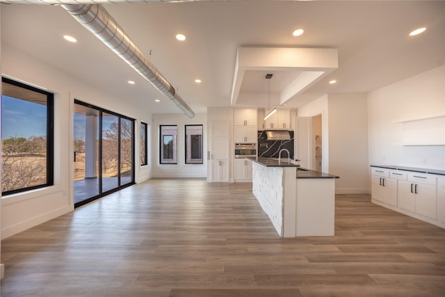 kitchen with open shelves, recessed lighting, light wood-style floors, white cabinets, and a kitchen island with sink