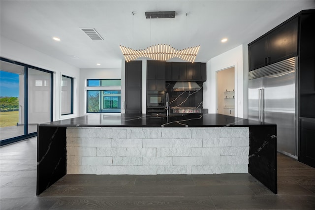 kitchen with stainless steel built in fridge, exhaust hood, visible vents, decorative backsplash, and dark countertops