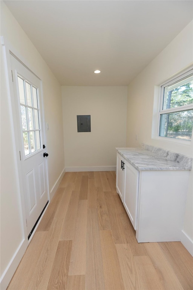 clothes washing area with light wood-style flooring, recessed lighting, electric panel, and baseboards