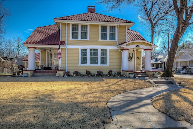 mediterranean / spanish-style home featuring a tiled roof, a porch, a chimney, and a front lawn