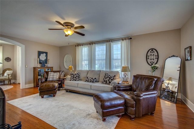 living room featuring a ceiling fan, baseboards, arched walkways, and wood finished floors