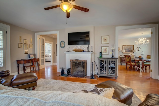 living room featuring a fireplace with flush hearth, ceiling fan with notable chandelier, baseboards, and wood finished floors