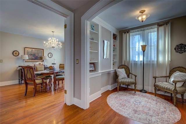 living area with an inviting chandelier, built in shelves, baseboards, and wood finished floors