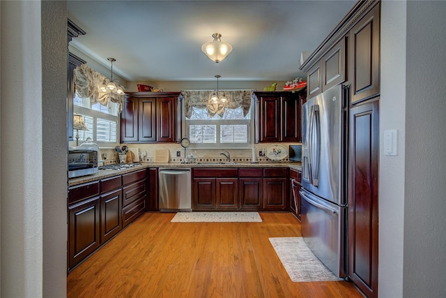 kitchen featuring appliances with stainless steel finishes, hanging light fixtures, light wood finished floors, and an inviting chandelier