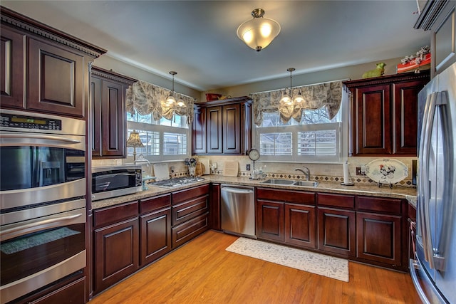 kitchen with a chandelier, a sink, light wood-style floors, hanging light fixtures, and appliances with stainless steel finishes