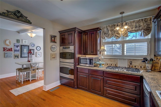 kitchen with visible vents, light wood-style flooring, appliances with stainless steel finishes, pendant lighting, and backsplash