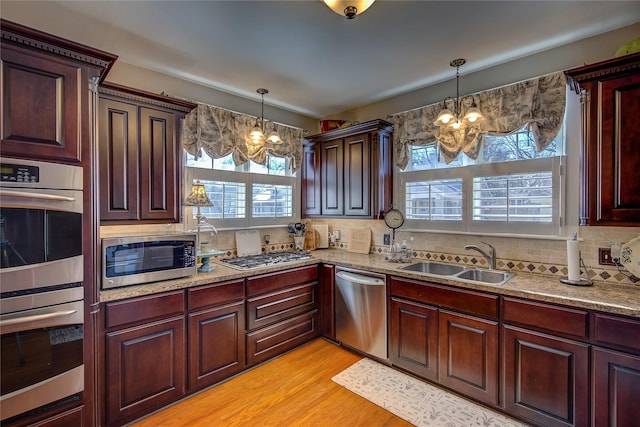 kitchen featuring a chandelier, stainless steel appliances, a sink, light wood-type flooring, and decorative backsplash