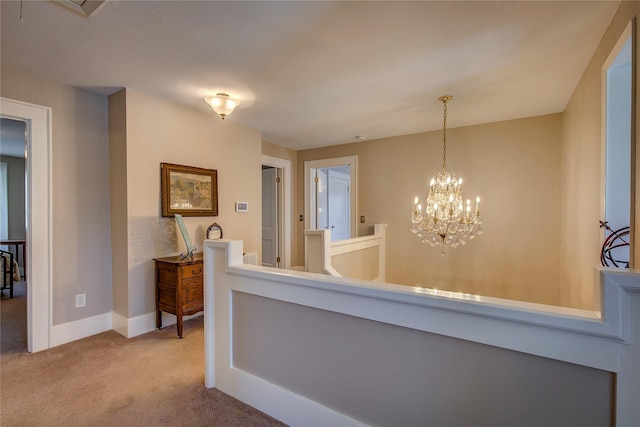 hall with carpet floors, a chandelier, baseboards, and an upstairs landing