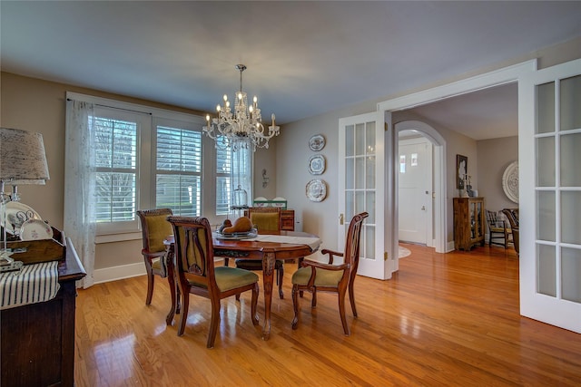 dining space featuring baseboards, french doors, light wood-type flooring, and an inviting chandelier