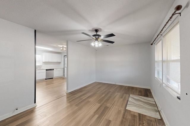 spare room featuring light wood-style floors, a ceiling fan, baseboards, and a textured ceiling