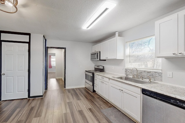 kitchen with wood finished floors, appliances with stainless steel finishes, a sink, and white cabinetry